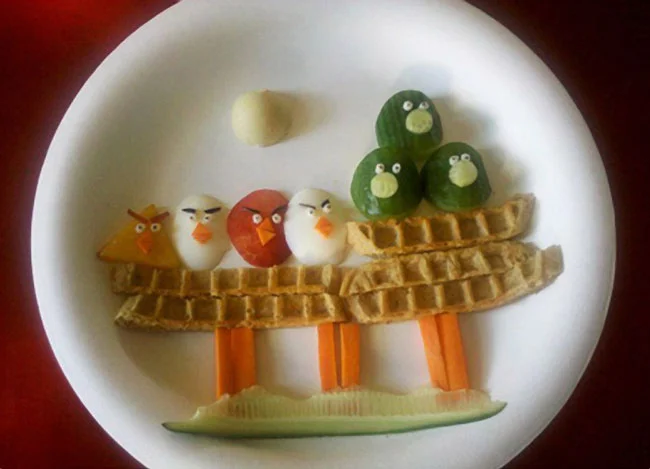 A creative plate of Angry Birds food art, recreating the game's birds and pigs from breakfast ingredients.