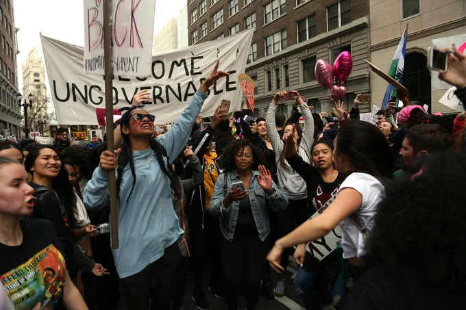 Demonstrators march through a city carrying a 'Become Ungovernable' banner, illustrating the slogan's use in real-world protest movements.