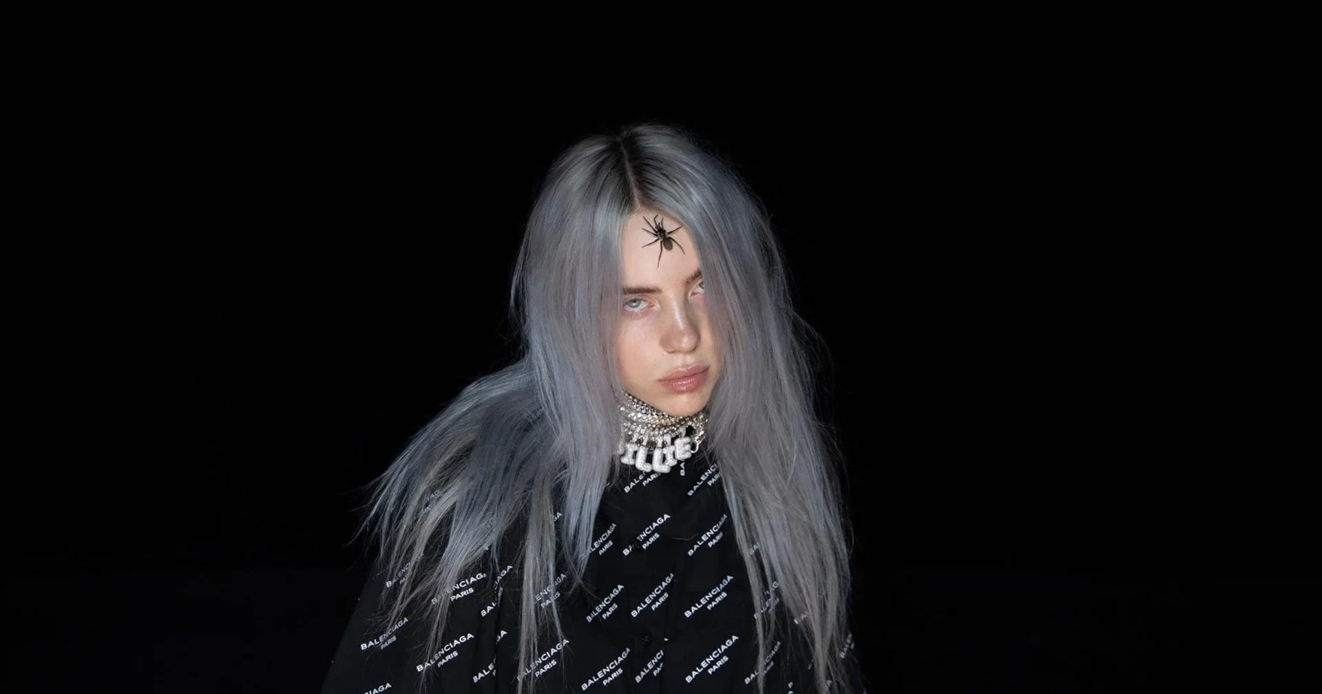 Billie Eilish in a signature moody portrait featuring silver hair, a spider on her forehead, and Balenciaga apparel.