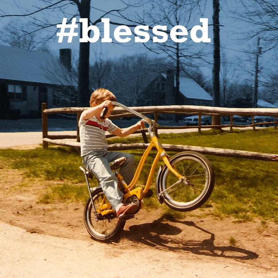The '#blessed' hashtag overlaid on a nostalgic photo of a boy doing a bike wheelie, illustrating the meme's ironic use to celebrate mundane moments of triumph.