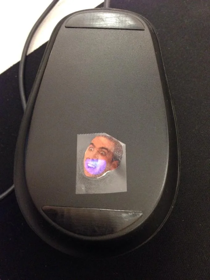 A subtle office caging: a Nicolas Cage face sticker applied to a coworker's computer mouse.