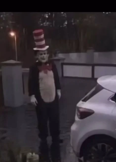A blurry sighting photo of the 'Cat in the Hat' stalker standing near a residential driveway, shared widely on TikTok and Snapchat.