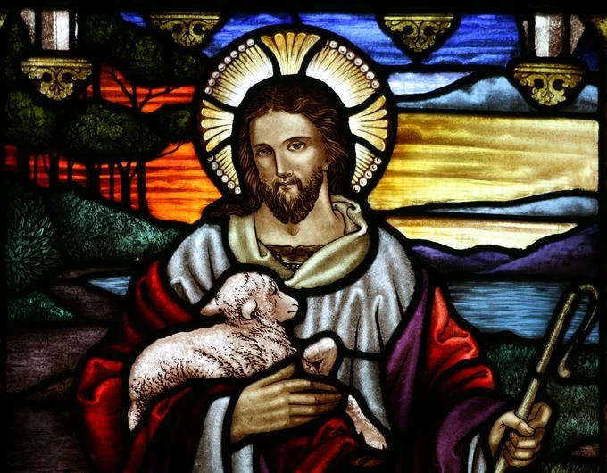 A traditional stained-glass depiction of Jesus as the Good Shepherd, a classic image of Christian iconography.