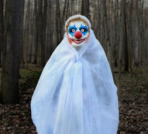 A staged creepy clown sighting photo depicting a masked figure lurking in the woods, evoking the 2016 clown scare panic.