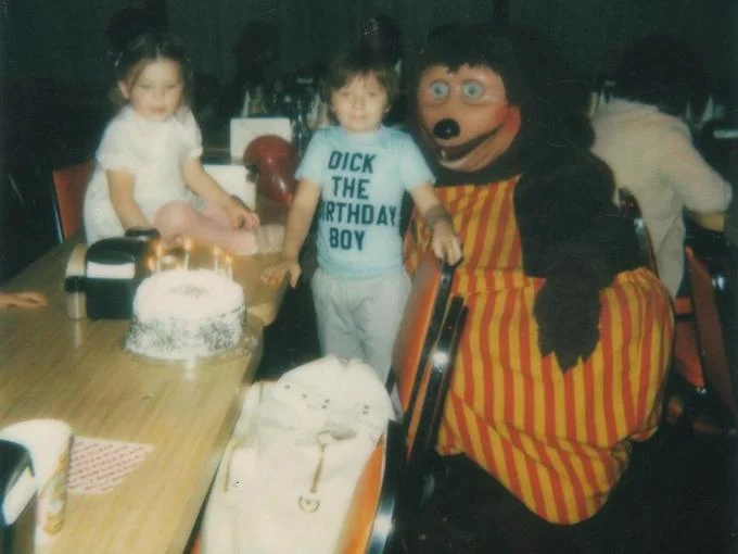 The full uncropped source photograph, revealing more of the party scene including a wrapped gift and the birthday cake with lit candles.