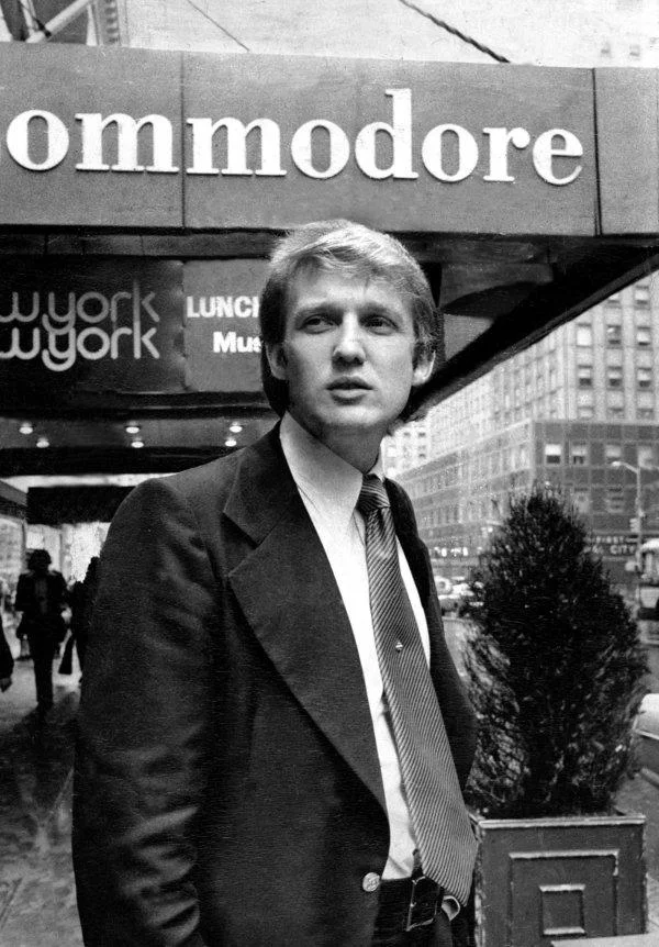 A young Donald Trump outside the Commodore Hotel in the 1970s, displaying his original hairstyle before it evolved into its famously blonde and elaborate later form.