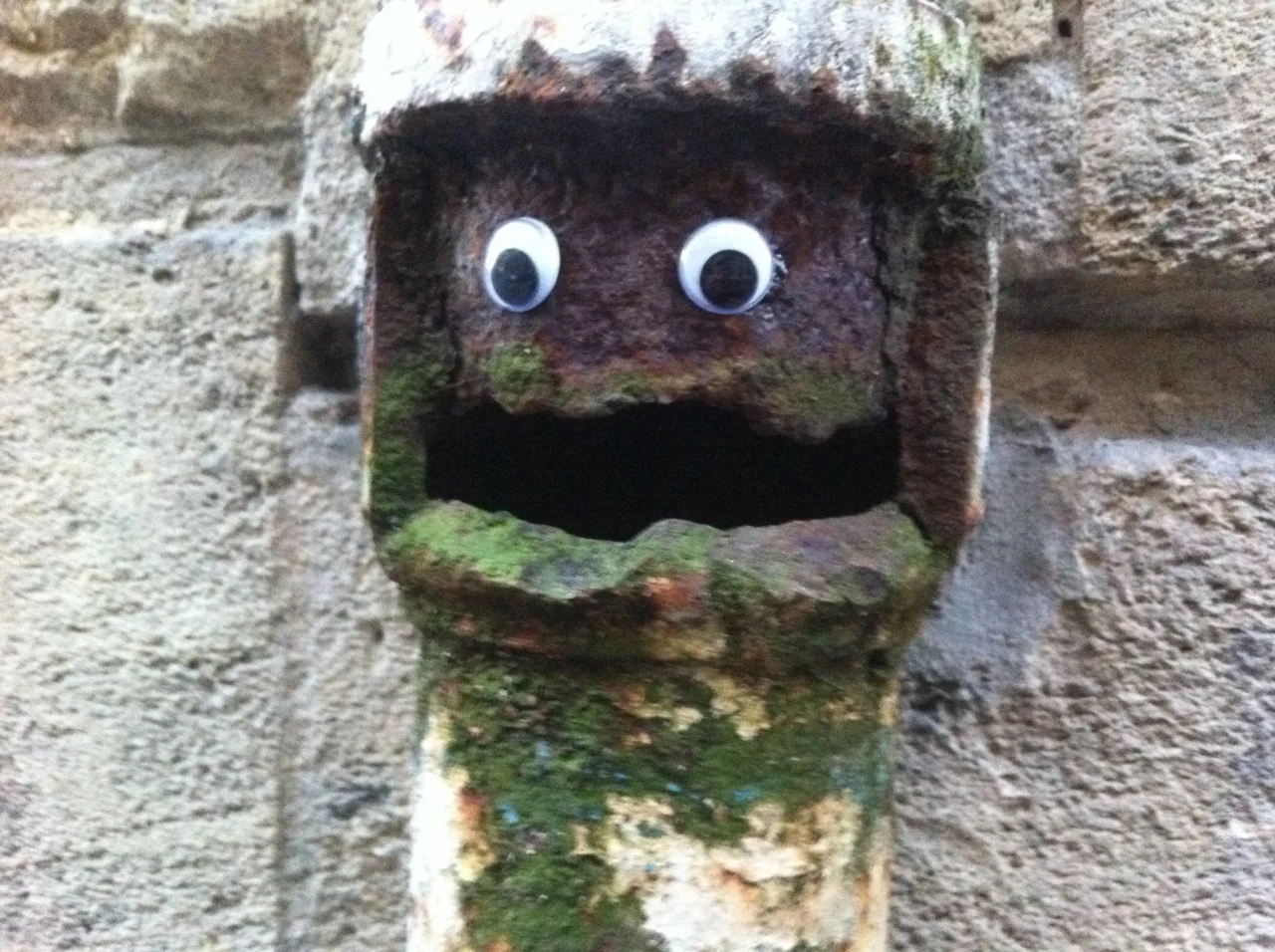 Classic example of eyebombing: googly eyes transform a weathered drainpipe into a smiling character.
