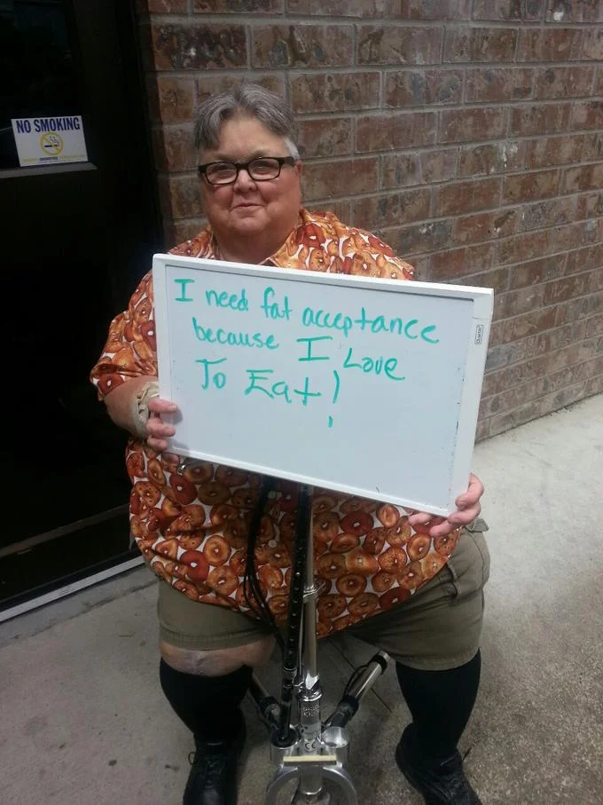 Another participant in the 'I Need Fat Acceptance Because' photo series, holding a handwritten sign expressing her reason for supporting the movement.