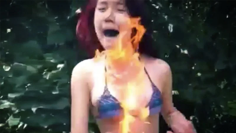 A still from a viral Fire Challenge video showing a participant with flames spreading across her chest and neck.
