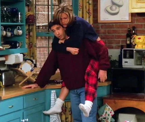 Ross carries Rachel piggyback through Monica's kitchen in a memorable Friends scene.
