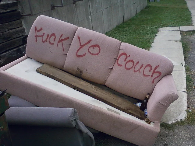 A discarded couch tagged with graffiti on a city street, a real-world example of the meme's spirit.