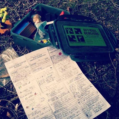 A found geocache containing swag items and a logbook full of signatures from previous finders.