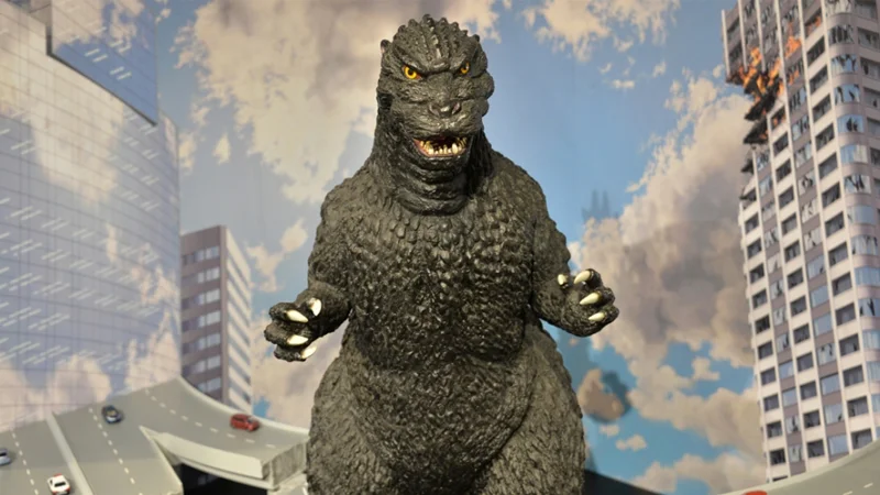 Godzilla, the towering kaiju created by Toho, depicted in a classic diorama pose in front of a burning city.