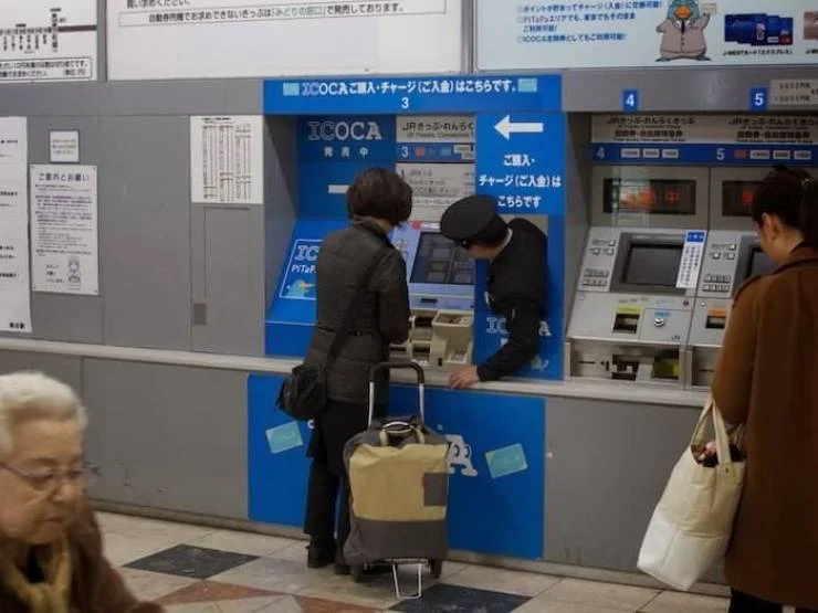 A JR station attendant assisting a passenger at an ICOCA IC-card ticket machine, showcasing Japan's customer service culture.