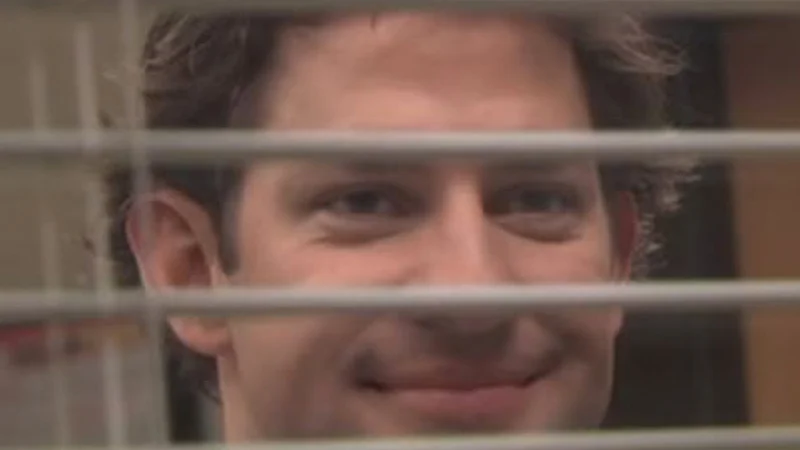 The original still of Jim Halpert (John Krasinski) smiling through the blinds, the source image for the meme template.