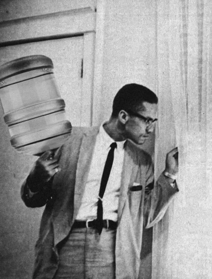A meme edit replaces the rifle in the famous Malcolm X 'By Any Means Necessary' photograph with a water jug, referencing the meme's protest symbolism.