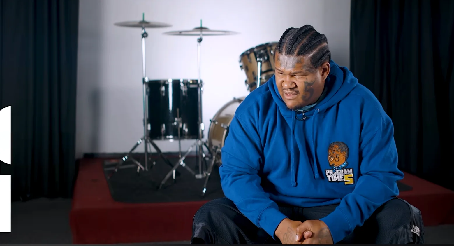 Screenshot from the interview associated with the 'Kalani Bear That's My Baby' meme, featuring the subject seated on an interview set with a drum kit backdrop.