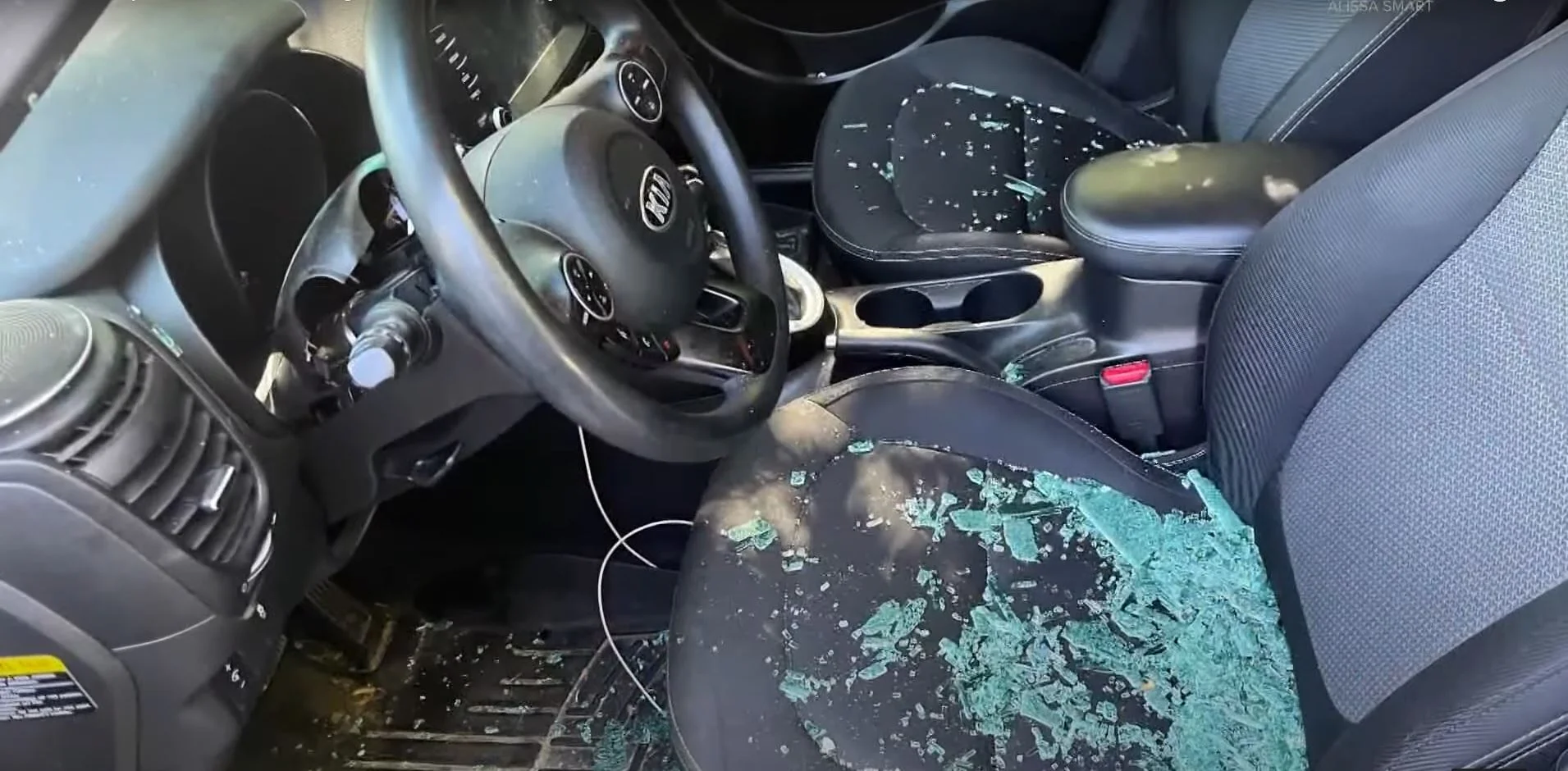 The aftermath of a Kia Challenge theft attempt: a smashed window, a stripped steering column and ignition, and broken glass covering the driver's seat.