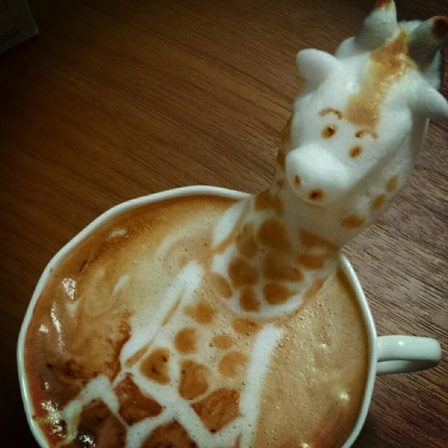 A three-dimensional latte art giraffe stretching its neck up from the foam surface of a cappuccino.
