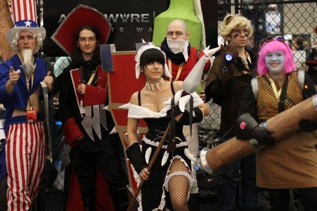 Cosplayers portraying champions Fiddlesticks, Gragas, Olaf, and Amumu at the Riot Games convention booth.