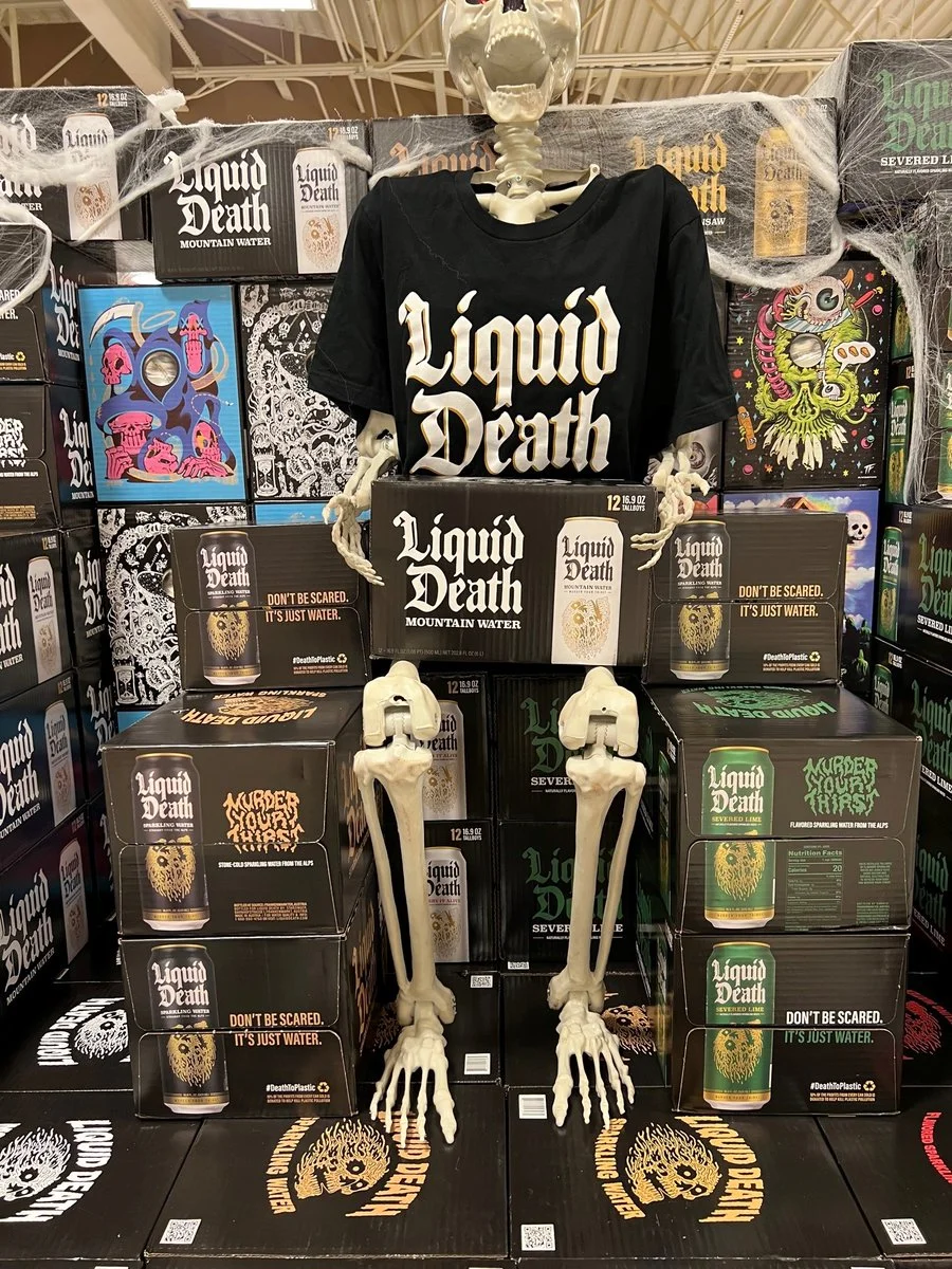 A retail Halloween display showcasing Liquid Death's heavy-metal aesthetic, complete with a skeleton mascot sporting the brand's t-shirt.