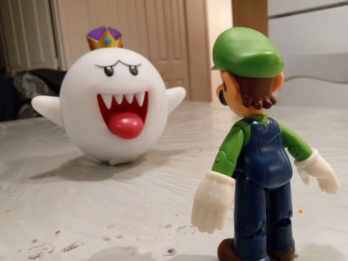 A photograph of collectible Luigi and King Boo figures staged in a face-off pose.