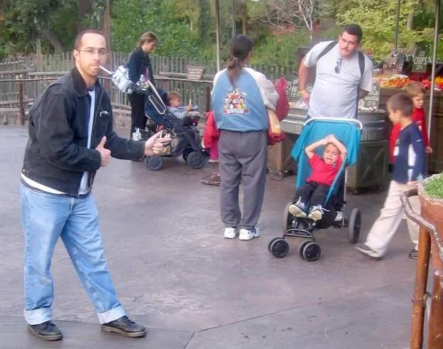 A child imitates the Lynndie England pose next to a woman talking on the phone, demonstrating the meme's spread as amateur photo humor.
