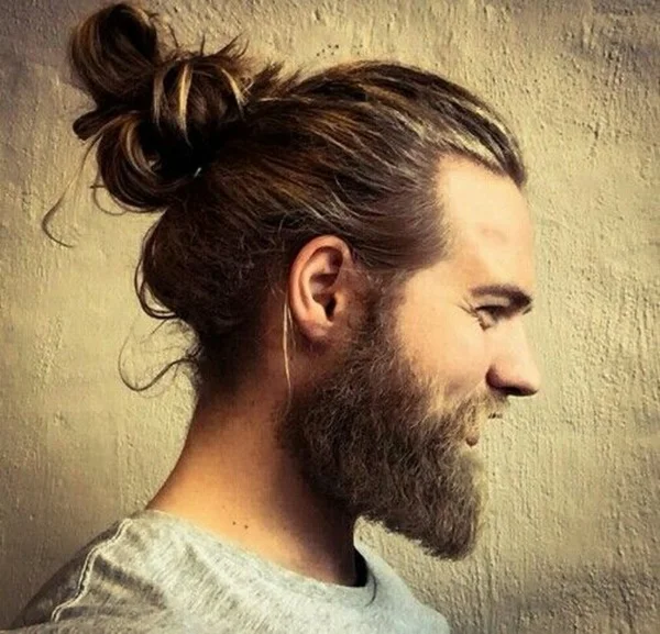 The classic look associated with the man-bun trend: long hair gathered into a top-of-the-head bun, paired with a full beard.