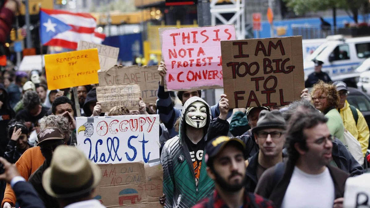 Occupy Wall Street protesters march through lower Manhattan carrying handmade signs, including a demonstrator in a Guy Fawkes mask holding a 'Too Big To Fail' placard.