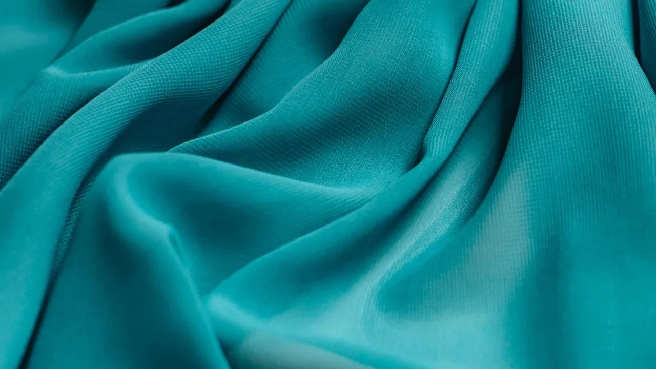 Close-up of teal polyester fabric, used as the icon representing the 'polyester' slang term popularized on TikTok.