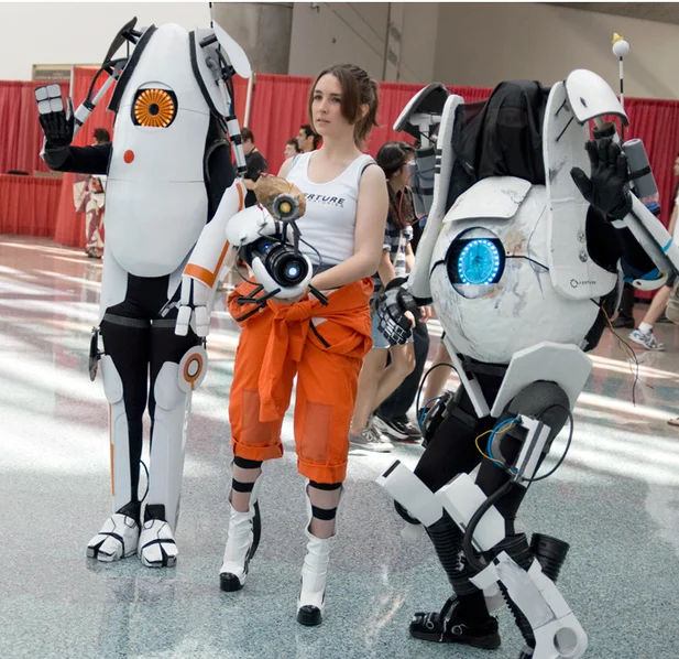 Portal cosplayers depicting Chell alongside the cooperative robots Atlas and P-Body at a convention.