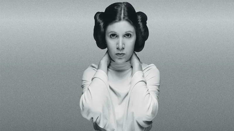 Carrie Fisher as Princess Leia in the character's iconic white robe and hair-bun hairstyle from Star Wars.