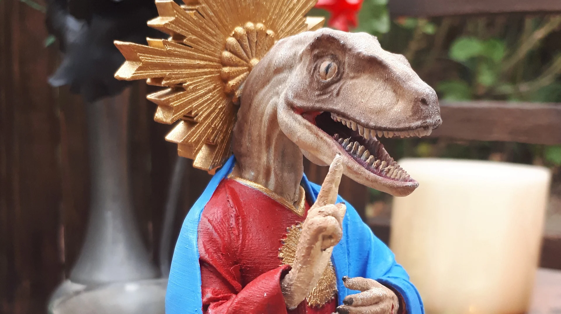 A 3D-printed collectible figurine of Raptor Jesus, blending traditional Sacred Heart iconography with a velociraptor head.