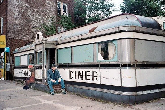 A photoshop edit placing Sad Kanye next to a lonely figure outside a retro urban diner, extending the meme's melancholy tone.