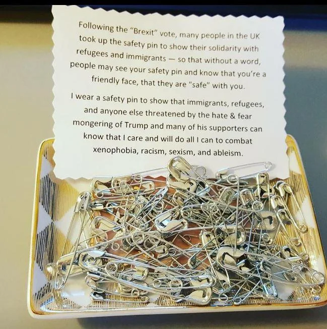 A dish of safety pins with an explanatory note offered as a way for supporters to take one and visibly show allyship against xenophobia and racism.