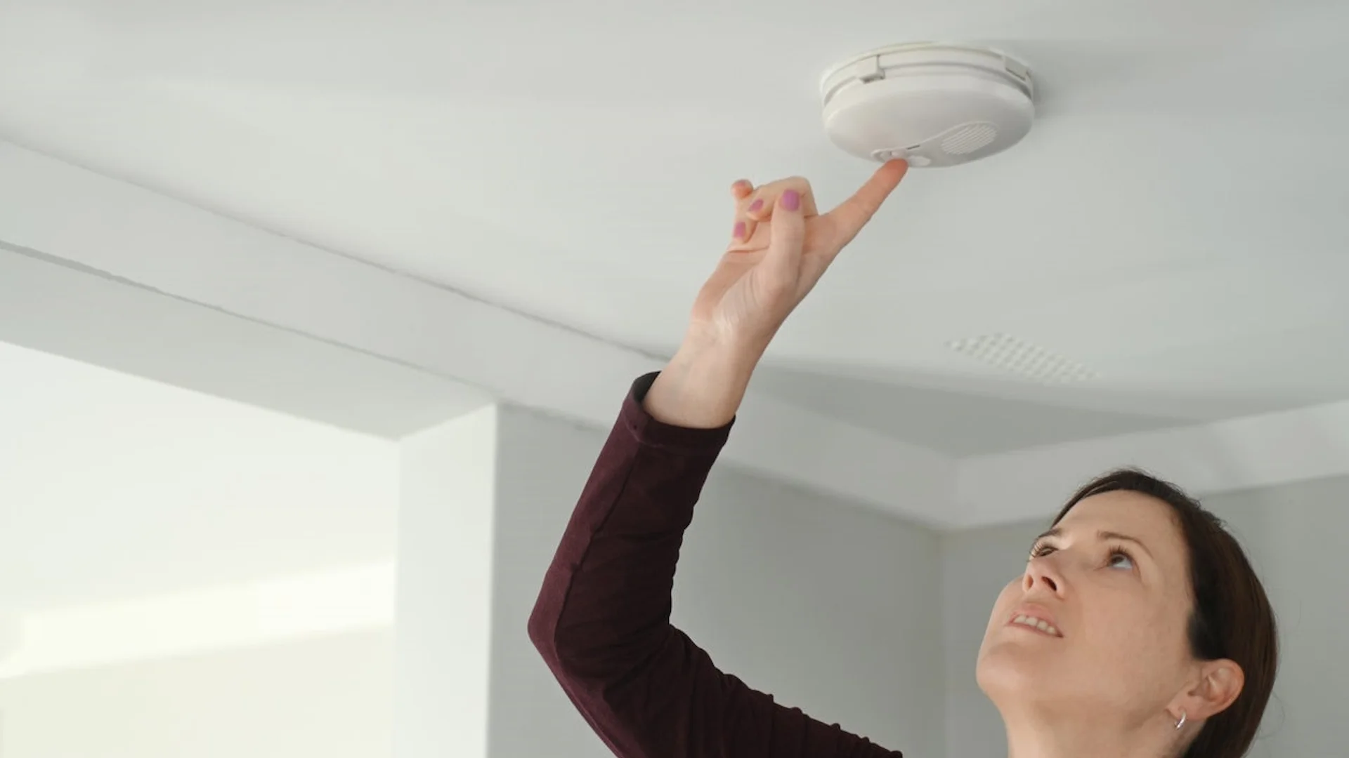 A woman tests a ceiling smoke detector, the type of alarm at the center of the 'smoke detector beeping' meme.