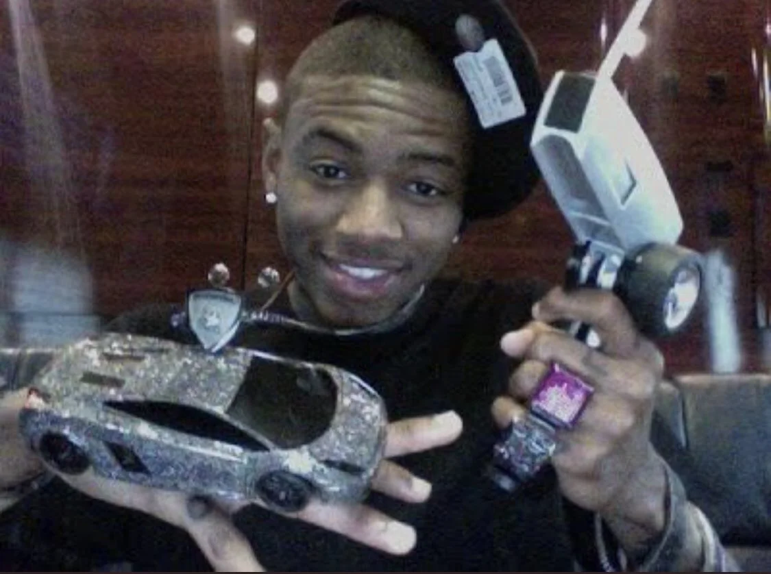 An early-career Soulja Boy showing off a diamond-covered miniature Lamborghini and rhinestone camera, an image often shared to highlight his signature 'swag' aesthetic.
