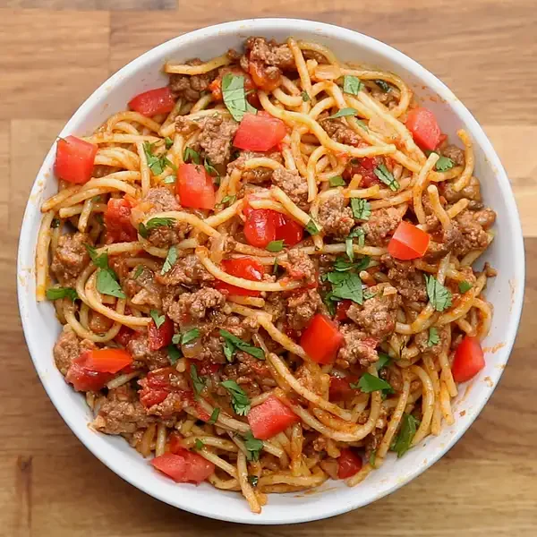 A stylized BuzzFeed food video still showing a bowl of spaghetti with fresh basil and parmesan.