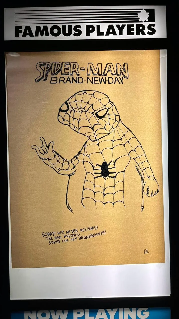 A hand-drawn Spoderman-style Spider-Man: Brand New Day poster displayed in a Famous Players movie theater with an apology note for missing official promotional materials.