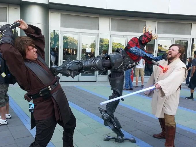 Star Wars cosplayers reenacting a Clone Wars-era duel between Jedi and Sith characters at a fan convention.