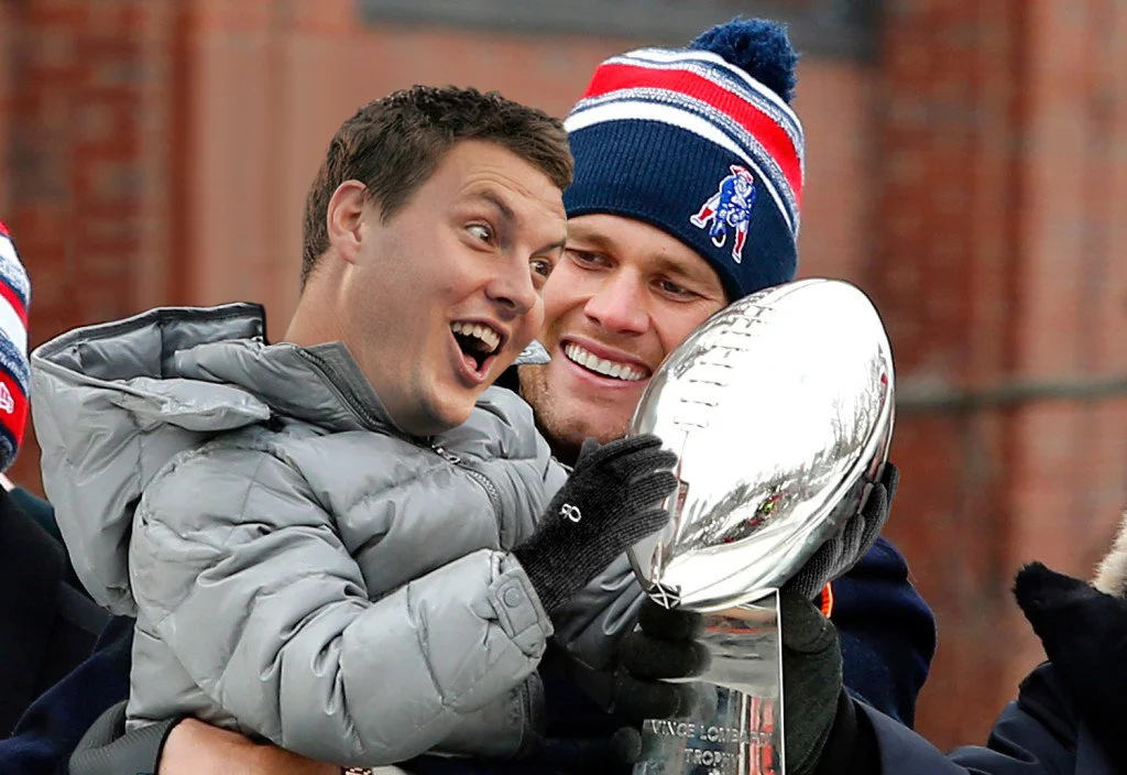 Tom Brady celebrates a Super Bowl victory while holding the Vince Lombardi Trophy during a Patriots championship parade.