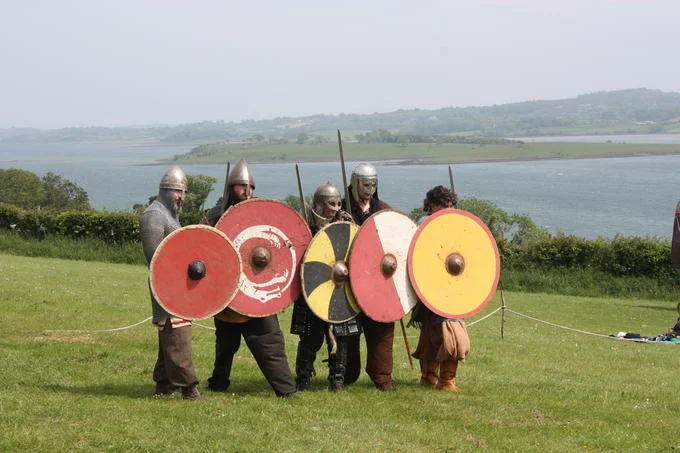 Modern Viking reenactors demonstrate shield wall formation with authentic round shields and period attire during a historical reenactment event.