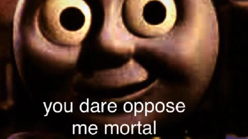 The original 'you dare oppose me mortal' image template, featuring a cursed close-up of Thomas the Tank Engine captioned with the signature phrase.
